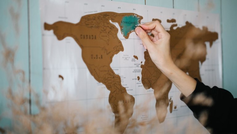 Hand scratching a colorful scratch off travel map showing visited countries and travel adventure