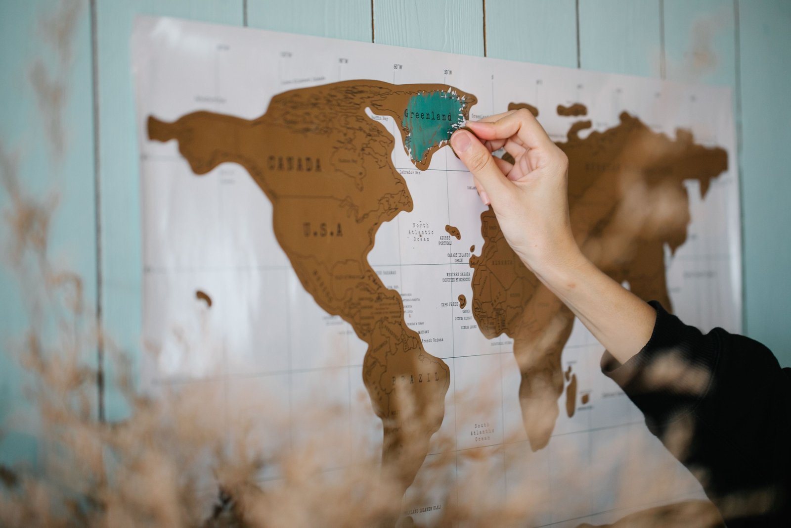 Hand scratching a colorful scratch off travel map showing visited countries and travel adventure