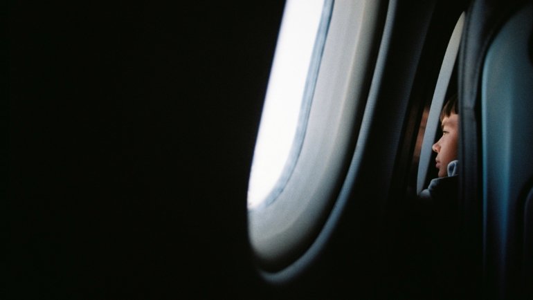 Child resting comfortably on airplane seat using a colorful children’s travel pillow for neck support