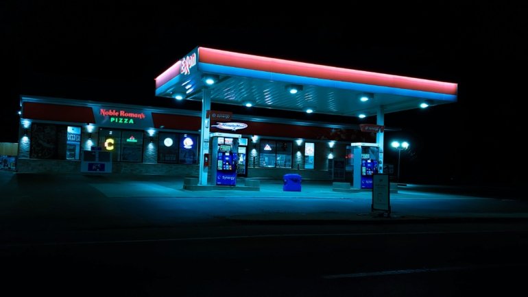 24 seven travel plaza at night with fuel stations, convenience store, and resting travelers on a highway road trip