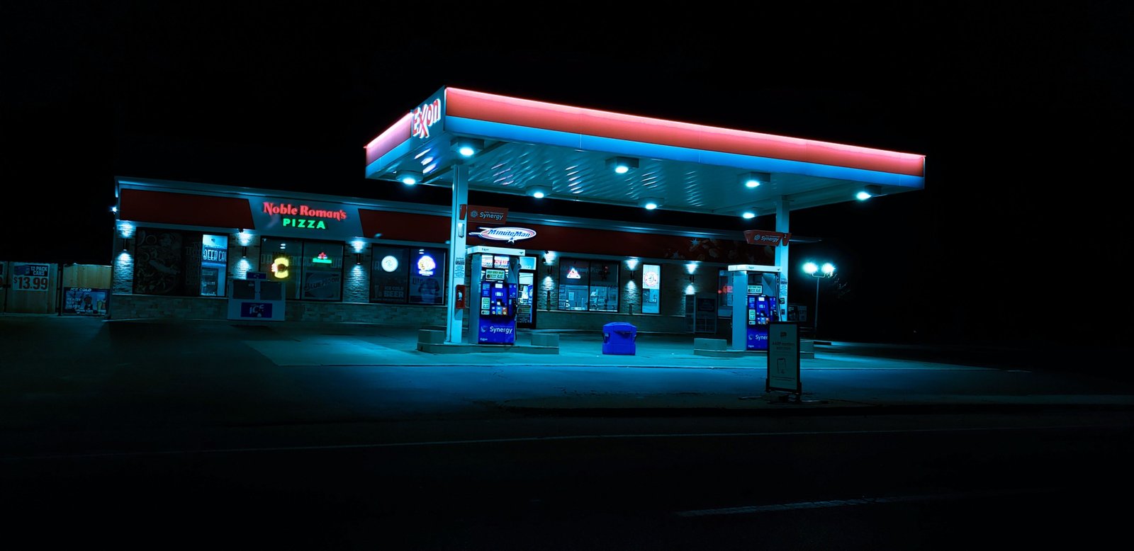 24 seven travel plaza at night with fuel stations, convenience store, and resting travelers on a highway road trip