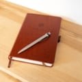 Leather bound travel diary open with pen on wooden table, symbolizing durable and stylish travel journaling companion