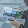 Traveler holding a Maine travel guide book with scenic coastal and forest landscape in the background