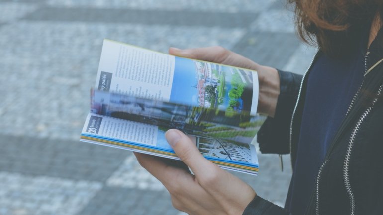 Traveler holding a Maine travel guide book with scenic coastal and forest landscape in the background