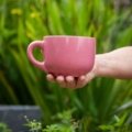 Pink stainless steel travel coffee mug outdoors, reusable and leak-proof with bright color, perfect for commuting and travel