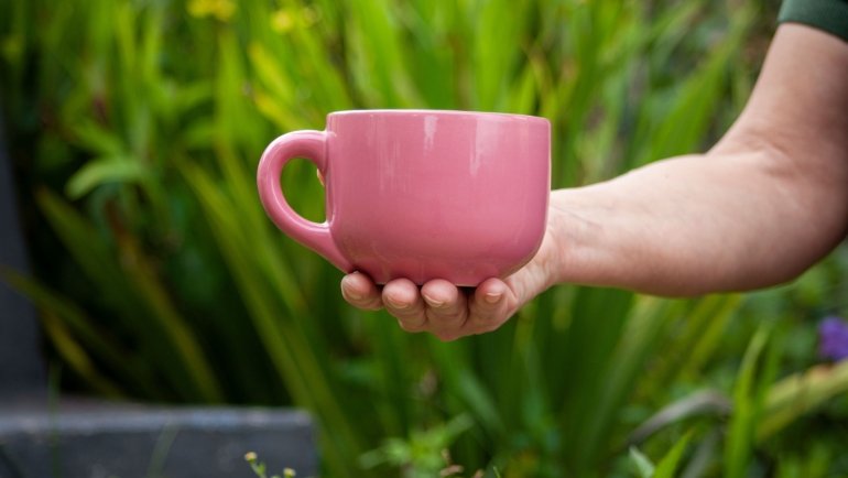 Pink stainless steel travel coffee mug outdoors, reusable and leak-proof with bright color, perfect for commuting and travel