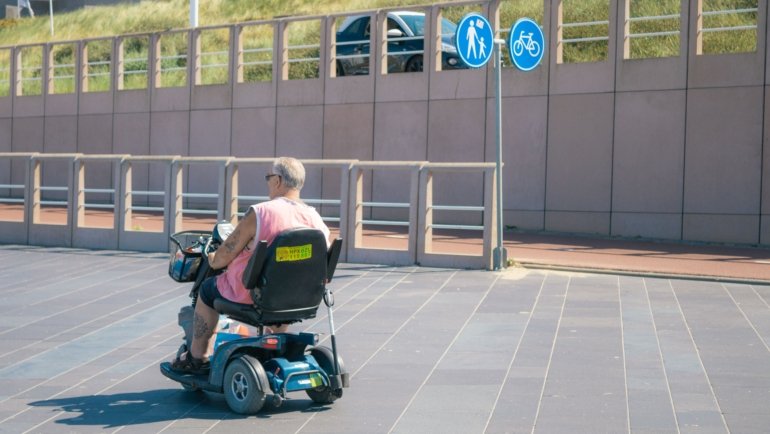 Lightweight portable travel disability scooter used by a traveler outdoors for easy and independent mobility