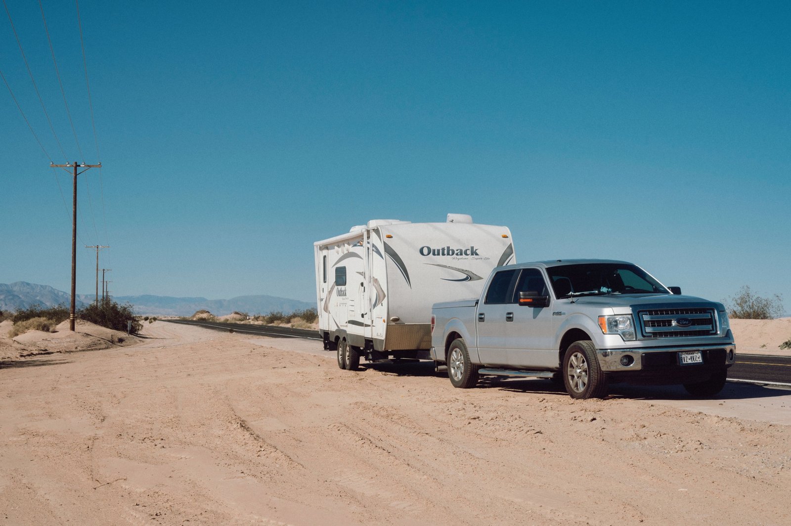 Lightweight toy hauler travel trailer parked outdoors with motorcycles, showcasing compact living and garage space for outdoor adventures