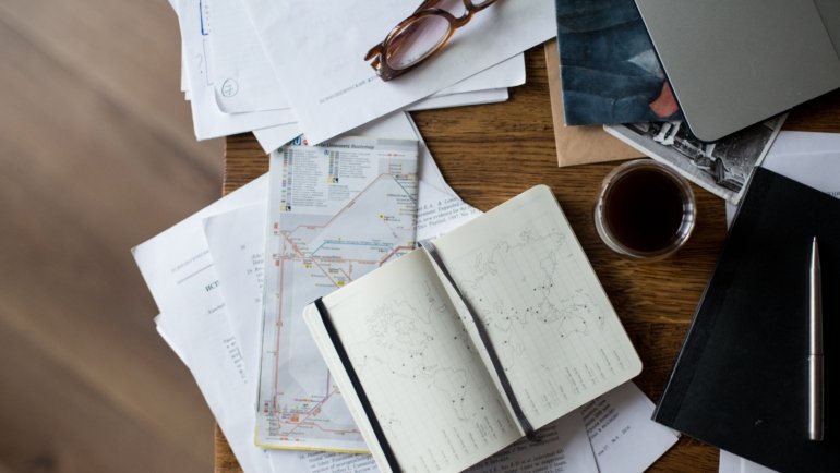 Person planning a trip on laptop with travel maps and guides for flight, accommodation, and itinerary organization