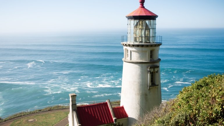 Scenic view of Oregon Coast beach with lighthouse and dramatic cliffs under clear sky