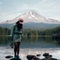 Travel nurse standing outdoors with Oregon landscape and hospital in background, representing travel nursing career and adventure
