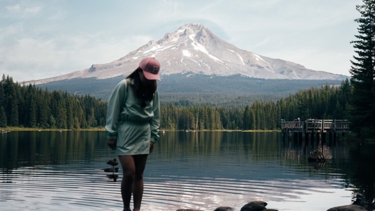 Travel nurse standing outdoors with Oregon landscape and hospital in background, representing travel nursing career and adventure