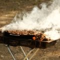 Portable travel smoker cooking outdoors during a camping trip, showcasing convenience and smoky flavors on the go