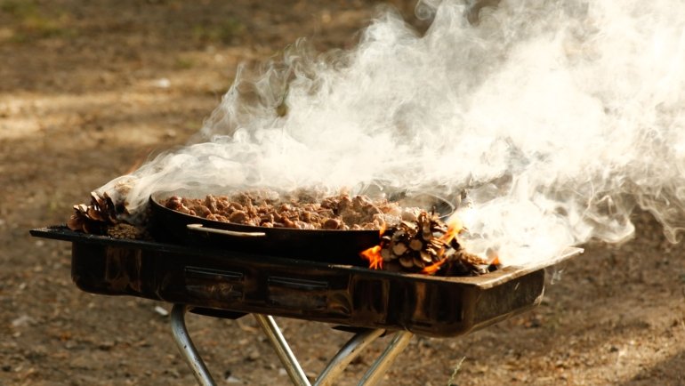 Portable travel smoker cooking outdoors during a camping trip, showcasing convenience and smoky flavors on the go
