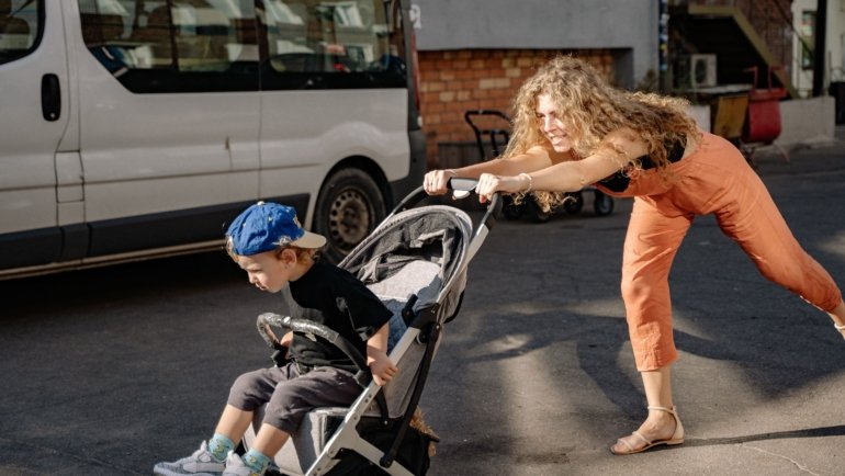 Parent pushing Joie stroller travel system with baby outdoors in a park