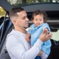 Parent carrying a padded travel bag protecting a baby car seat during family trip