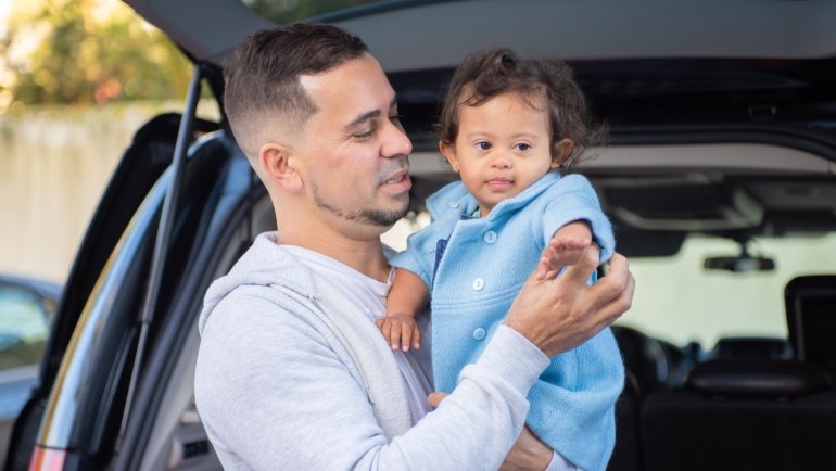 Parent carrying a padded travel bag protecting a baby car seat during family trip