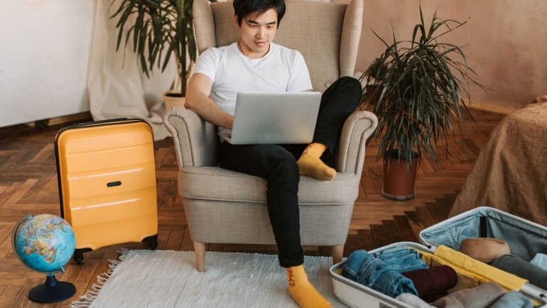 Traveler planning a trip online using Globequest Travel platform on laptop, surrounded by travel materials