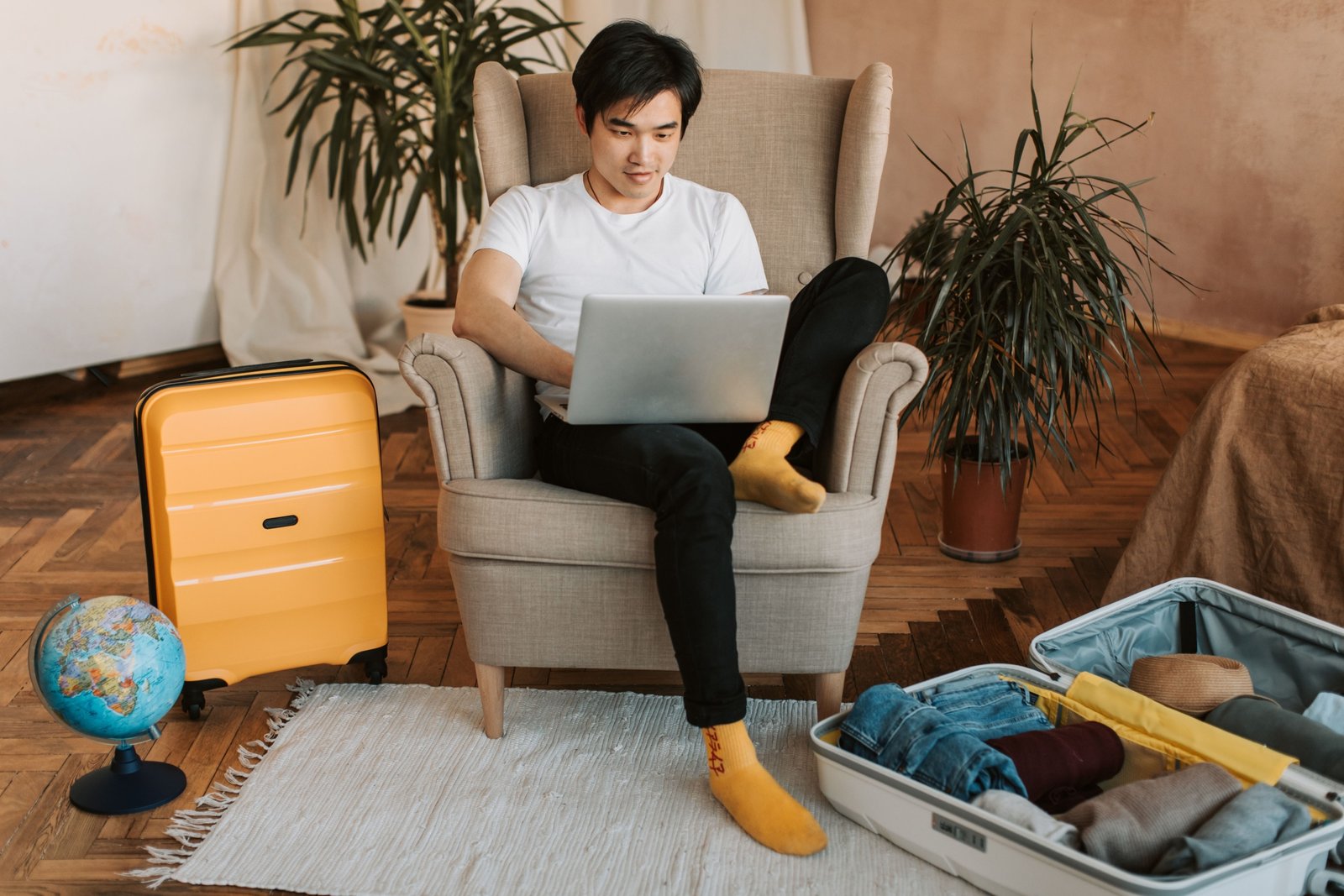 Traveler planning a trip online using Globequest Travel platform on laptop, surrounded by travel materials