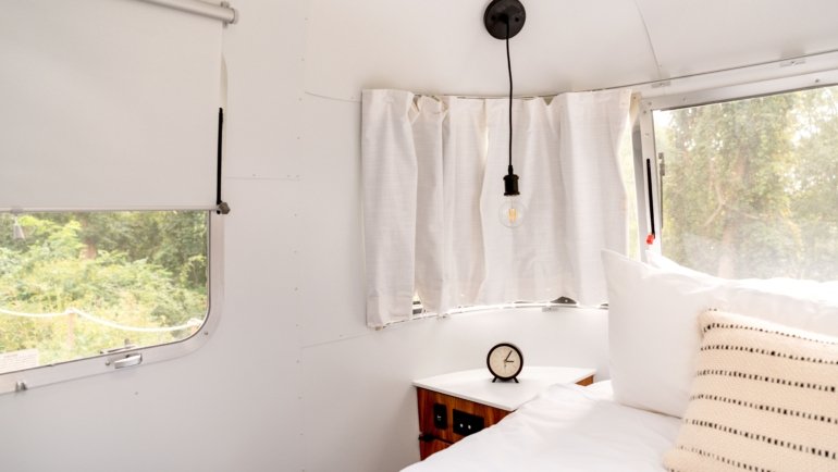 Interior of a rear living room travel trailer with panoramic windows and comfortable seating area overlooking nature