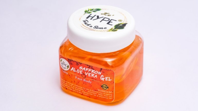 Travel size aloe vera gel bottle next to backpack and sunglasses for soothing and moisturizing skin care on the go