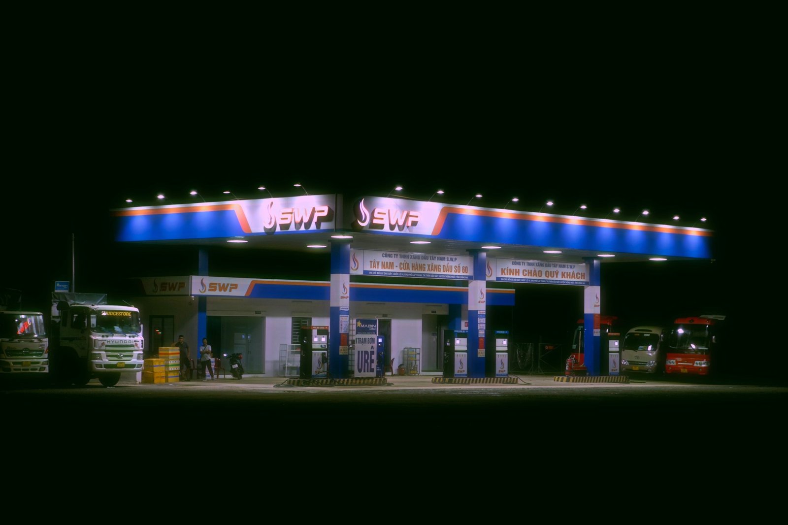 Modern commercial truck stop with trucks parked, fuel pumps, and traveler amenities for long-haul drivers