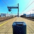 Lightweight rolling luggage and backpacks at a European train station platform with passengers preparing for train travel