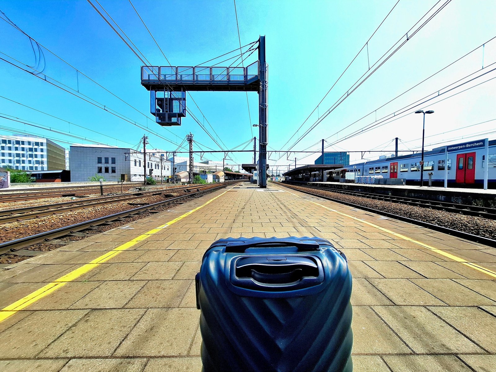 Lightweight rolling luggage and backpacks at a European train station platform with passengers preparing for train travel