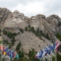 Tourists visiting Mt Rushmore National Memorial during a guided travel package tour with clear blue skies and scenic Black Hills backdrop