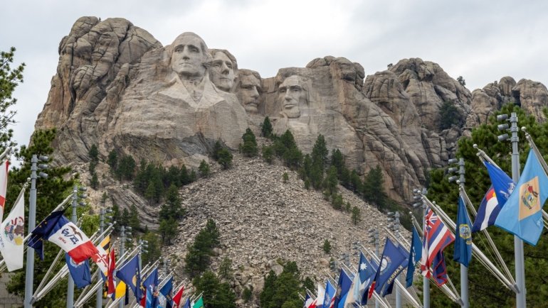 Tourists visiting Mt Rushmore National Memorial during a guided travel package tour with clear blue skies and scenic Black Hills backdrop