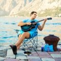 Foldable travel guitar being played outdoors by a traveler, highlighting portability and convenience for musicians on the go