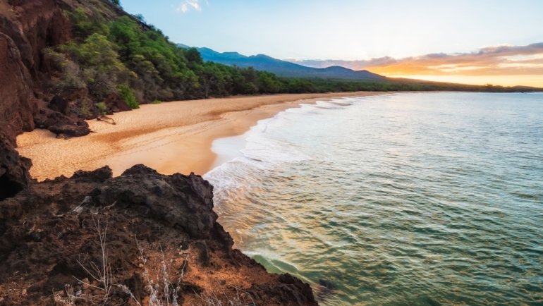 Beautiful Maui tropical beach at sunset with calm ocean waves and lush green landscape