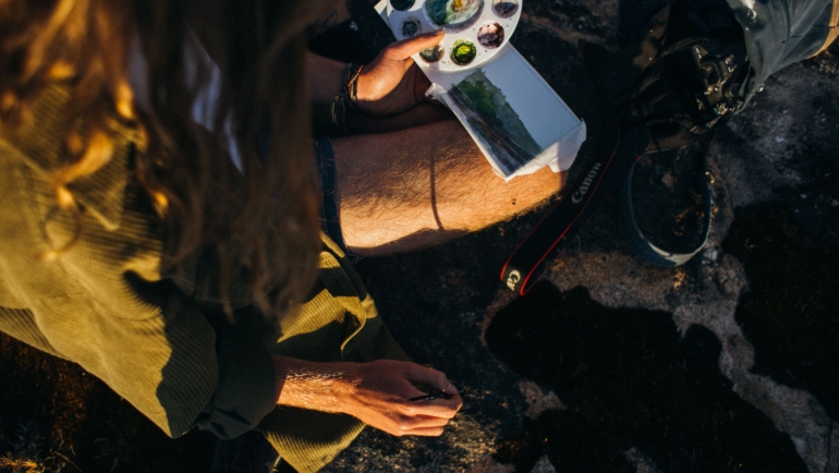 Artist using a compact watercolor travel set to paint outdoors in nature, illustrating portable watercolor painting on the go
