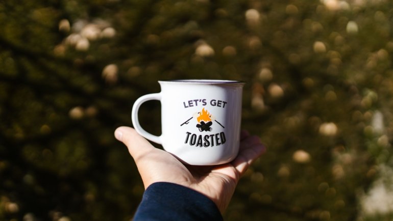 Funny travel mug with humorous quote held by traveler outdoors, showcasing personality and joyful morning routine