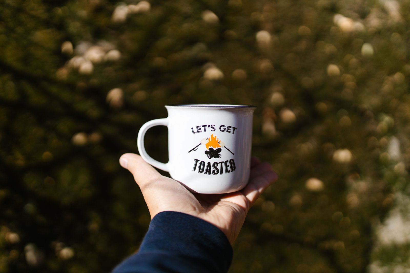 Funny travel mug with humorous quote held by traveler outdoors, showcasing personality and joyful morning routine