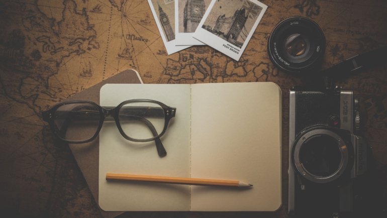 Open A5 traveler's notebook with pen surrounded by travel accessories including a map, camera, and passport