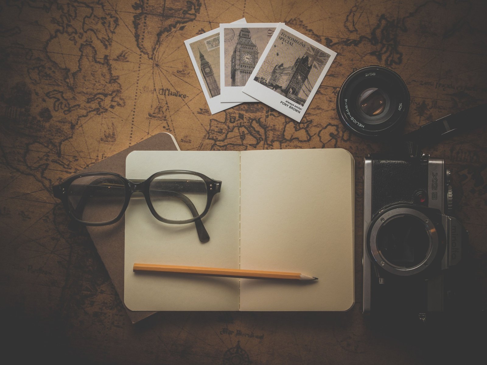 Open A5 traveler's notebook with pen surrounded by travel accessories including a map, camera, and passport