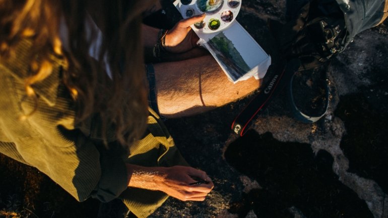 Artist using a travel watercolor kit to paint outdoors during a journey